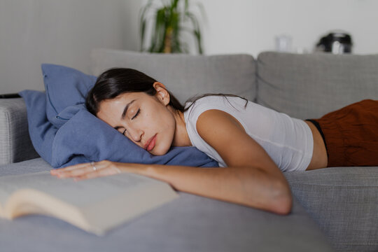 Exhausted young woman sleeping peacefully on a cozy sofa, enjoying a moment of tranquility after immersing herself in a captivating book