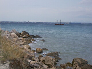 Rocks on the sea coast. A sailboat is sailing on the sea. Waves and stones
