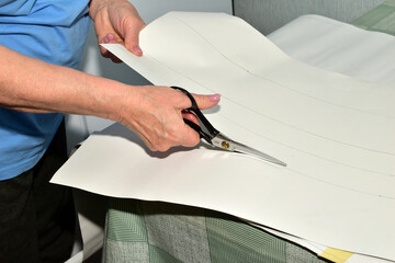 The cutter of clothing cuts out a pattern of clothing details with scissors from paper.