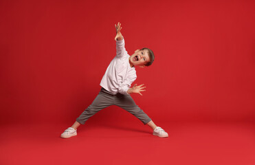 Happy little boy dancing on red background, space for text