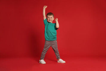 Happy little boy dancing on red background, space for text