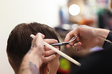 Professional barber cutting client's hair with scissors in barbershop, closeup