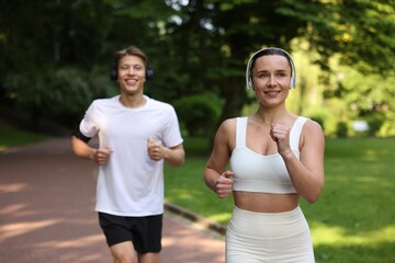 Sporty couple with headphones running in park, selective focus