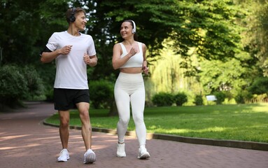 Sporty couple with headphones running in park, space for text