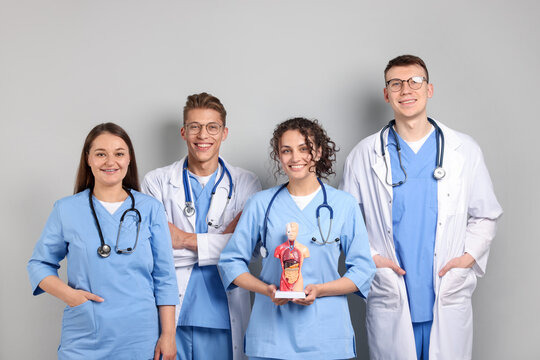 Group of medical students with human body model on light grey background