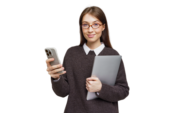 Engaging young adult in cozy sweater holding smartphone and laptop while smiling at the camera in a bright environment