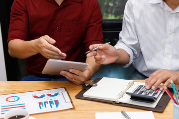 Close-up of hands working on a tablet and calculator, analyzing marketing data and financial performance. ธeam members review financial reports and charts, engaging in a precise business discussion.