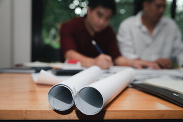 Rolled blueprints on a wooden table with blurred architects in the background discussing a project....