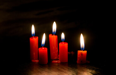 imagen con cinco velas rojas encendidas en un entorno oscuro. Tiene un estilo íntimo, ceremonial y...