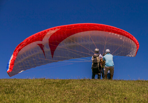 Preparaci&oacute;n para vuelo en parapente biplaza sobre colina con cielo despejado