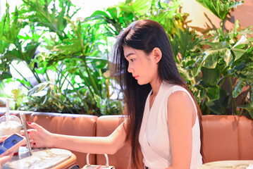 Asian Woman Using Smartphone in a Modern Caf&eacute; Surrounded by Plants