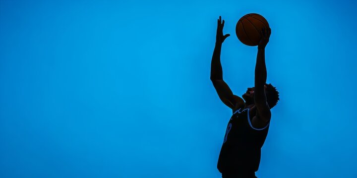 A basketball player in mid-dunking motion against a vibrant blue background, showcasing intense athleticism and dynamic energy.
