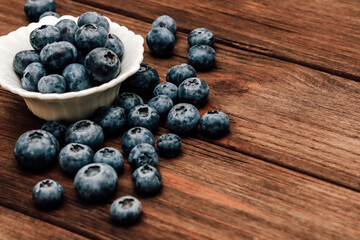 Fresh blueberries in a white bowl on a rustic wooden table at morning light