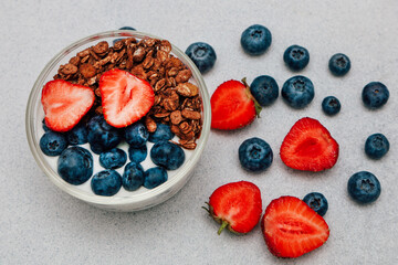 Bowl of yogurt granola and fresh berries on a gray surface with blueberries and strawberries