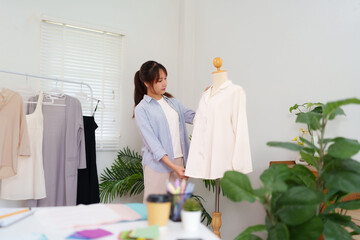 Young Asian Women Fashion Designer Adjusting Clothing on Mannequin in Studio Create New Collection...