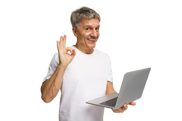 Smiling man in casual attire shows positive gesture while holding a laptop in a bright, transparent...