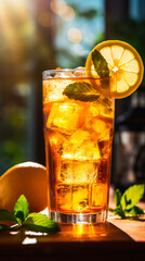 A refreshing glass of iced tea with lemon and mint on a wooden surface in bright sunlight bokeh background