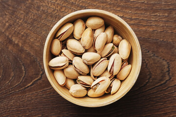 Bowl of pistachio nuts. Tasty salted snack in shell. Healthy protein food in rustic wooden bowl. Natural background with brown texture. Organic nutrition for active lifestyle.