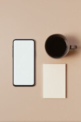 Minimalist flat lay of smartphone, coffee mug and notepad on neutral background