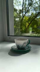 A beautiful porcelain cup and saucer sits on the windowsill