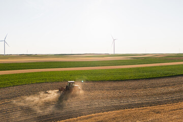 Agricultural tractor is working on the field with wind turbines. Aerial view