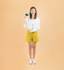 Asian young woman with a broken arm wrapped in bandages, representing the concept of purchasing accident insurance to protect against unexpected events, paid with a credit card.