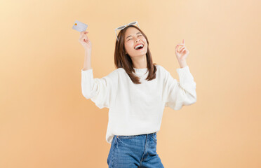 Cheerful beautiful Asian woman holding credit card isolated on beige color background.