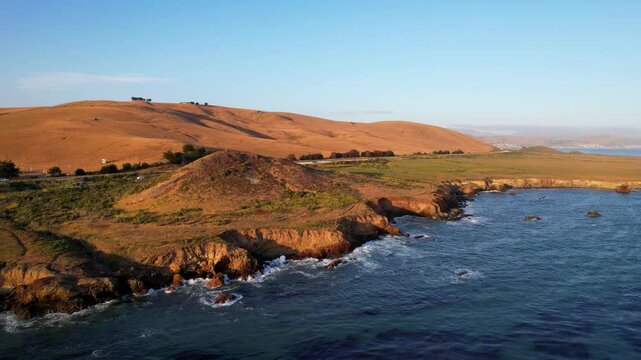 Aerial view of world famous Highway 1 Roadtrip West Coast California. Estero Bluffs State Park. Waves crashing against beautiful cliffs at sunset golden hour with highway running directly next to it