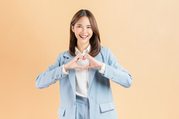 Smile Asian businesswoman making heart shape hand sign isolated against a beige background.