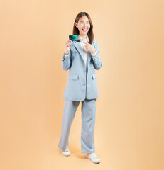 Cheerful beautiful Asian businesswoman holding credit card isolated on beige color background.