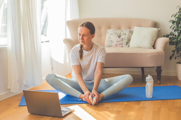 Young woman practicing yoga at home on a sunny day. Serene morning light streaming through the...