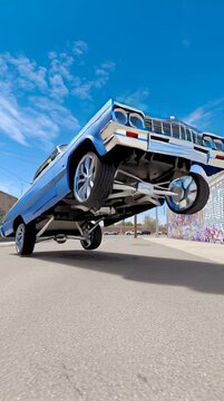A classic lowrider with a clean blue paintjob and rims hitting the hydraulic switches