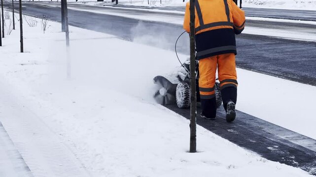 A man removes snow with a snow blower in the yard of a house in a snowy winter