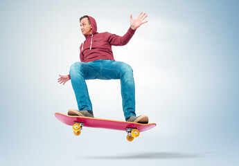 Young man in red hoodie and jeans jumps high on a red skateboard, performing a trick with...