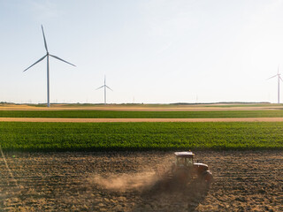 Agricultural tractor is working on the field with wind turbines. Aerial view