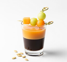 Fototapeta premium Espresso glass layered with cantaloupe juice, cantaloupe cubes, melon balls on cocktail picks, and seeds styled beside on white background