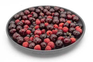 Cherry, raspberry and currant composition on a black plate on a white background - close-up of a berry composition