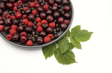 Cherry, raspberry and currant composition on a black plate on a white background - close-up of a berry composition