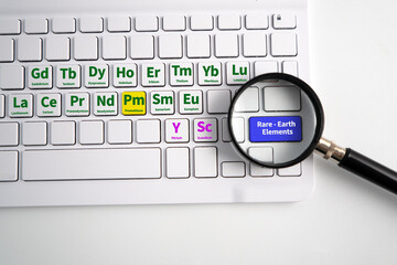 17 rare-earth elements symbol and name labeled on keyboard’s 17 keys. A loupe hovering over a...