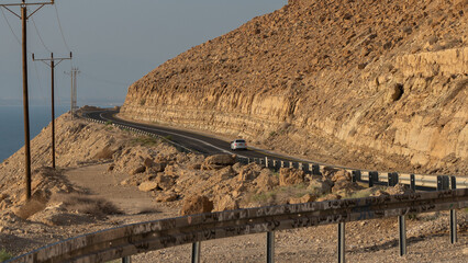Curved Desert Road Along Cliffs Near the Dead Sea with Power Lines and Blue Sky