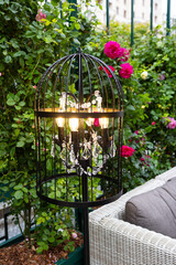 Decorative lantern in the garden. The lantern is made in a black checkered color and is surrounded by bright pink roses and green foliage.