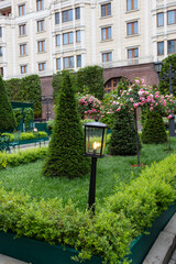 Decorative lantern in the garden. The lantern is made in a black checkered color and is surrounded by bright pink roses and green foliage.
