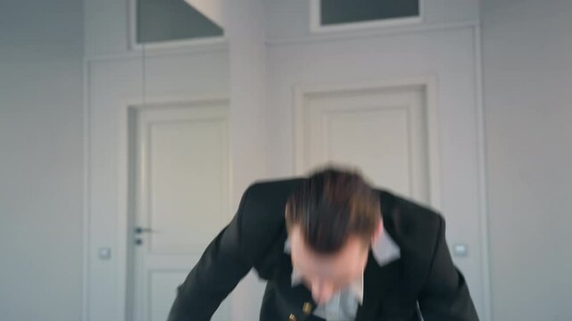 melodramatic male dancer in long black coat begins to fall toward ground mid-performance, arms raised expressively, dramatic movement framed by minimalist white studio background