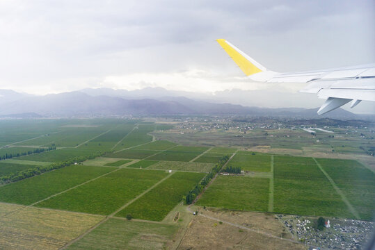 Travel to Montenegro: approaching Podgorica airport. View from airplane window during descent over agricultural fields and mountain valley. Aerial landscape with farmland and rural settlement