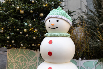A cheerful snowman stands in a festive urban setting. Decorated with elegant Christmas trees and twinkling lights, creating the atmosphere of a winter holiday.