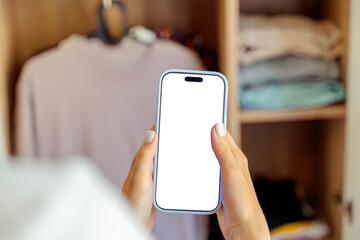 Woman using smartphone with blank screen in front of organized wardrobe