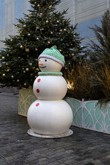 A cheerful snowman stands in a festive urban setting. Decorated with elegant Christmas trees and twinkling lights, creating the atmosphere of a winter holiday.