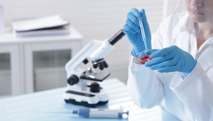 Scientist working with sample in Petri dish at table in laboratory, closeup