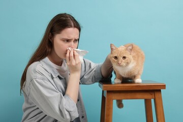 Woman suffering from allergy with her cat on light blue background
