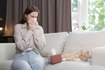 Woman suffering from allergy with her cat on sofa at home